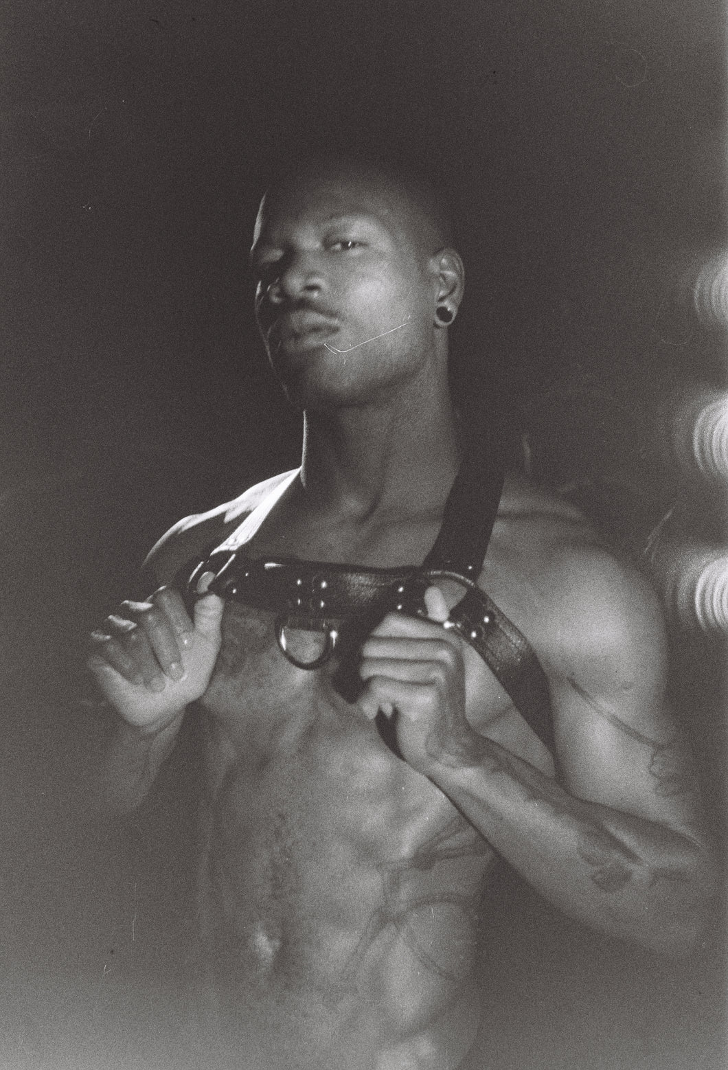 Bishop black modeling. On the front, a strap runs across the top part of the chest (with a D-ring for those who want to attach other gear!), while two side straps run under the arms and above the shoulders. On the back, the item fastens through two buckles on the lower strap, which connects to the neckpiece through a single strap running vertically across the top of the back.